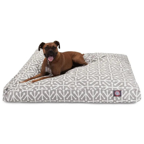 A brown dog lounges on the Majestic Pet Aruba Rectangle Dog Bed, which has a raised, angled side, plush polyester fiber fill, a machine washable cover, and a small logo tag on the corner. The dog looks ahead with its tongue out.