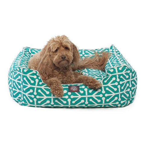 A fluffy brown dog relaxes in the Majestic Pet Aruba Contemporary Lounge Bed, featuring a teal and white pattern with raised sides.