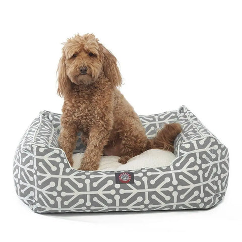 A curly-haired brown dog sits on a white cushion inside the Majestic Pet Aruba Contemporary Lounge Bed, featuring a gray and white geometric pattern.