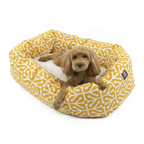 A small brown curly-haired dog lies in the Majestic Pet Aruba Sherpa Bagel Dog Bed, a yellow rectangular bed with a white bone pattern, raised sides, a soft white cushion, and water-resistant fabric for easy cleaning.