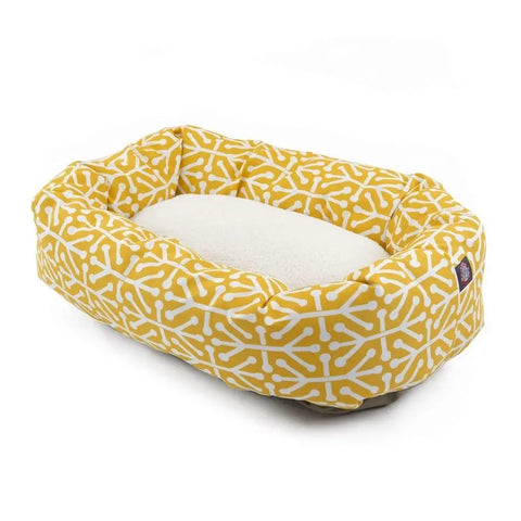 The Majestic Pet Aruba Sherpa Bagel Dog Bed features a yellow and white geometric bone pattern, a plush white cushion, and water-resistant fabric—combining comfort, style, and easy cleaning for your pet.