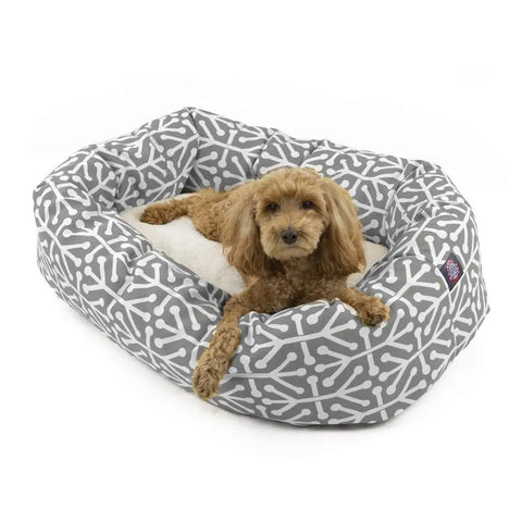 A small brown dog with curly fur relaxes in the Majestic Pet Aruba Sherpa Bagel Dog Bed, featuring water-resistant fabric, a plush white cushion, and a stylish white bone pattern.