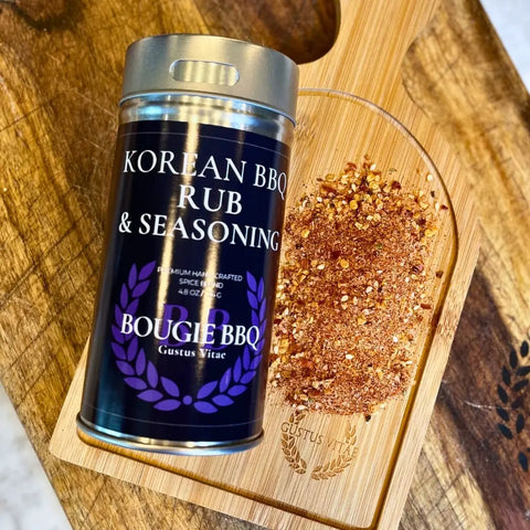 A tin from the Gustus Vitae Asian BBQ Seasonings Collection - 3 Pack sits on a wooden board with all natural seasonings, and a scoop cutout holds gourmet spice blends for the perfect Asian BBQ experience.