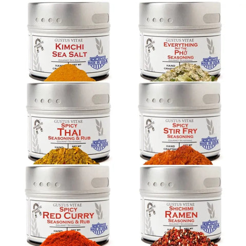 The Gustus Vitae Asian Seasonings Gift Set - Tastes of Asia features six artisanal spice blends: Kimchi Sea Salt, Everything Pho, Spicy Thai, Spicy Stir Fry, Spicy Red Curry, and Shichimi Ramen. Each tin is shown with a small pile of spice in front.