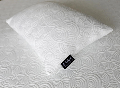 The Aslan Adjustable Pillow by Aslan Mattress, featuring a black Aslan tag, rests on a matching mattress. Both showcase a white, textured, embossed swirl design for coordinated style.