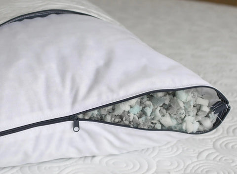 A close-up of the Aslan Adjustable Pillow by Aslan Mattress features its cool-to-the-touch, partially unzipped cover, revealing shredded memory foam filling inside. The pillow rests on a white, textured mattress.