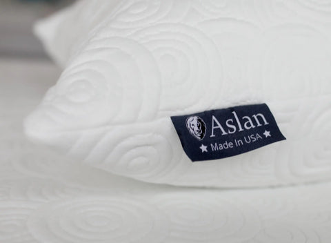 Close-up of the Aslan Adjustable Pillow by Aslan Mattress, featuring a white textured spiral pattern and a navy tag with the lion logo, two stars, and Aslan Made in USA.