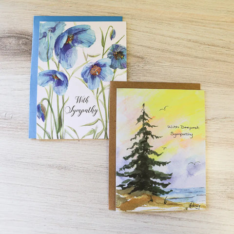 Part of the JuLu Cards Assorted Card Bundle, these sympathy cards feature blue flowers with With Sympathy text and a tree by water at sunset with With Deepest Sympathy text.