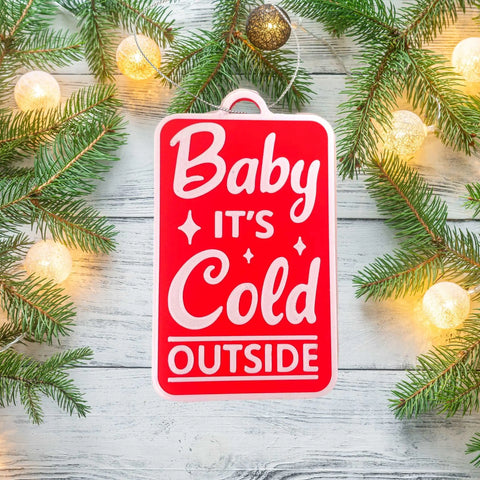 A red “Baby It’s Cold Outside Christmas Ornament” by Chatelet Manufacturing, made in the USA, features white text and festive charm—perfect for your holiday décor or Christmas tree.