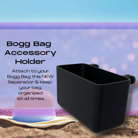 A black Chatelet Manufacturing BOGLETS organizer charm accessory, compatible with Bogg Bags, is displayed on a sandy beach with a pastel-striped sunhat. Ideal for keeping keys or personal items handy with your tote bag under a sunny sky.