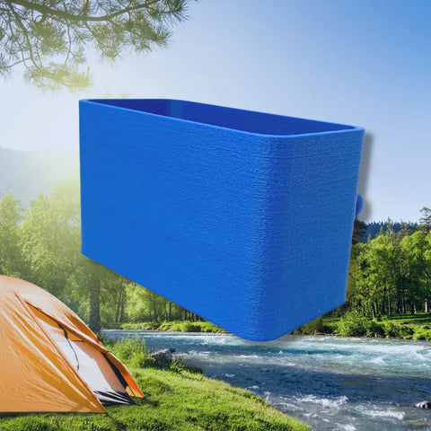 A BOGLETS organizer charm accessory by Chatelet Manufacturing, ideal for holding keys with your Bogg Bag, is shown floating above a riverside campsite featuring a yellow tent, green trees, and mountains beneath a clear blue sky.