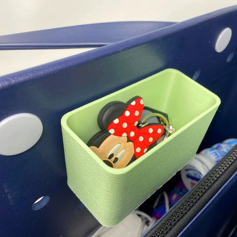 A BOGLETS Organizer Charm Accessory by Chatelet Manufacturing is attached inside a navy blue tote bag, keeping keys and personal items handy. A Minnie Mouse keychain with a red bow and white polka dots is clipped to the charm; other organizer items are nearby.