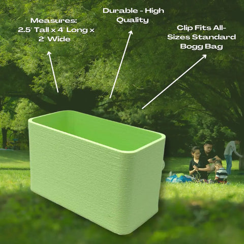 The BOGLETS Organizer Charm Accessory by Chatelet Manufacturing is a light green, rectangular 2.5x4x2 clip-on organizer for Bogg Bags—perfect for keys or small items. A family sits on the grass in a park in the background.
