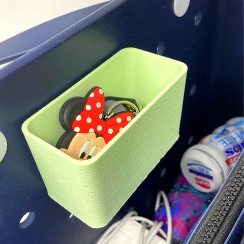 The BOGLETS Organizer Charm Accessory by Chatelet Manufacturing keeps your keys or personal items handy with your tote bag. Shown here in green, it holds a Minnie Mouse keychain and fits inside a navy polka dot tote alongside sanitizer and other essentials.