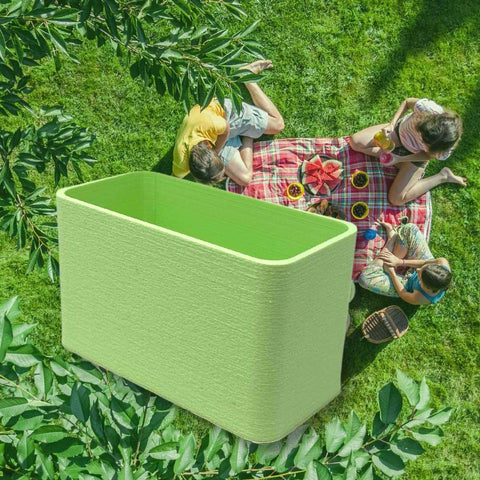 Three people sit on a picnic blanket with food on grass, surrounded by trees. A Chatelet Manufacturing BOGLETS Organizer Charm Accessory for Bogg Bags is digitally added to their green tote, keeping keys or personal items handy.