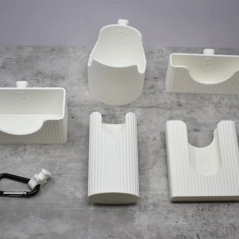 Five white, ribbed BAGLETS from Chatelet Manufacturing’s Premium Collection Ultimate Bundle, including a phone case, key & wallet holder, carabiner key holder, bottle accessory & sunglasses holder, are displayed on gray.