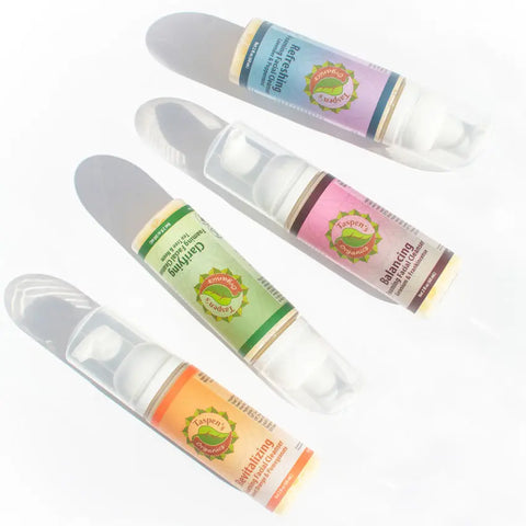 Four Taspens Organics cylindrical skincare bottles—blue (Refreshing), pink (Balancing Rose Geranium Foaming Facial Cleanser), green (Calming), and orange (Revitalizing)—are arranged diagonally on a white background with soft shadows.