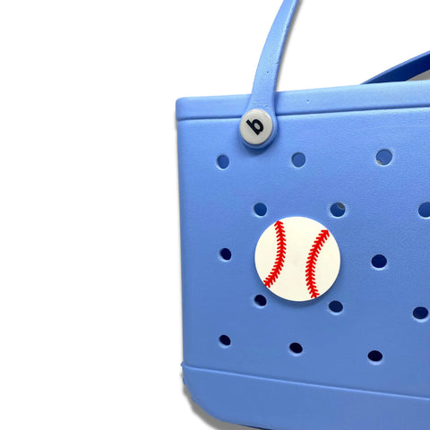 A close-up of a blue perforated bag with a white baseball sport charm and a “b” button on the handle, featuring Chatelet Manufacturing’s BOGLETS—Sport Charms for Rubber Beach Bags—backgrounded by white for unique customization.
