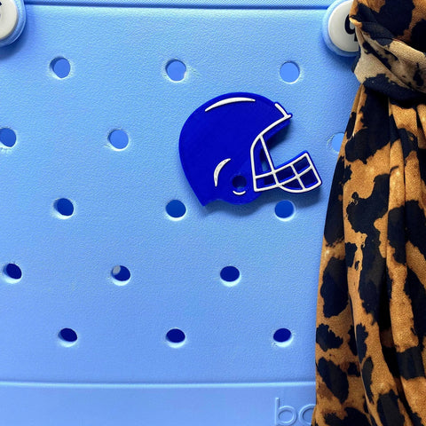 A blue football helmet BOGLET sport charm by Chatelet Manufacturing is shown on a light blue rubber beach bag, with brown and black leopard print fabric along the right edge. Perfect as an accessory for tote bags.