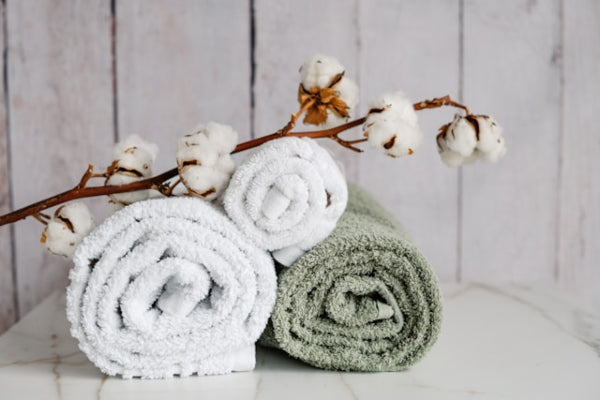 Two rolled towels, one white and one green, with a branch of cotton flowers on a wooden background.