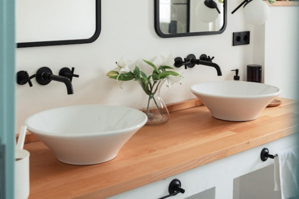 Bathroom vanity with two white sinks, black faucets, and a wooden countertop.