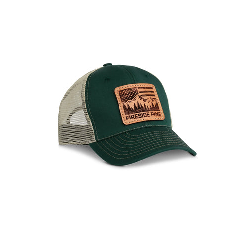 The Fireside Pine Battle Creek - Hunter Green/Khaki is a mesh-trucker snapback hat with a brown cowhide leather patch on the front, featuring a mountain, trees, and the text FIRESIDE PINE.
