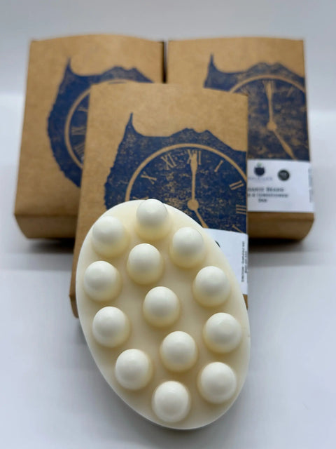 A white, oval Beard Wash & Conditioner Bar by Five O Clock Co., featuring raised bumps for massage, is shown in front of three brown boxes with a blue clock design—perfect for organic beard care.