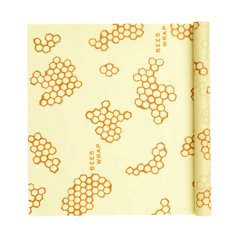 A Bees Wrap Roll, a customizable plastic wrap alternative, features an orange honeycomb pattern and “BEES WRAP” on a light yellow sheet—great for home bakers and cooks. One corner is partially rolled up.