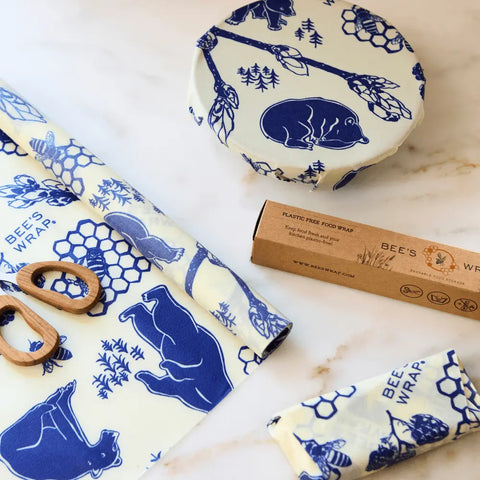 Bee’s Wrap Roll, a reusable food wrap from Bee’s Wrap, offers an eco-friendly alternative to plastic wrap—shown in blue bear and honeycomb designs beside a brown paper package and wooden-handled scissors on a white surface.