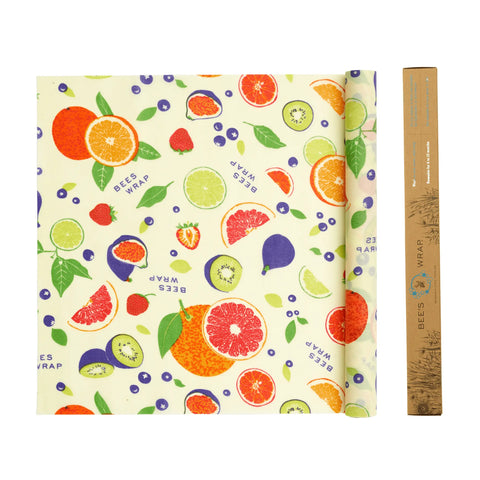 A folded Bee’s Wrap Roll with colorful fruit patterns—including oranges, limes, kiwi, berries, and leaves—sits beside its brown packaging tube. An eco-friendly plastic wrap alternative from Bee’s Wrap for home bakers.