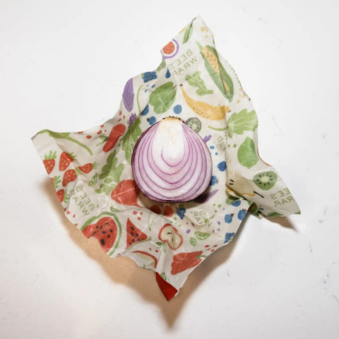 A halved red onion rests on Bees Wrap Assorted 3 Pack, colorful, plastic-free beeswax food wraps with fruit designs that help keep your food fresh.