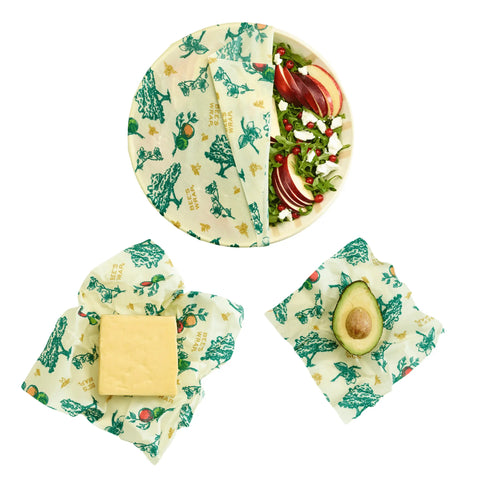 The Bees Wrap Assorted 3 Pack is pictured: one covers a salad bowl, another wraps cheese, and the third partially seals a halved avocado—keeping food fresh while reducing plastic use.
