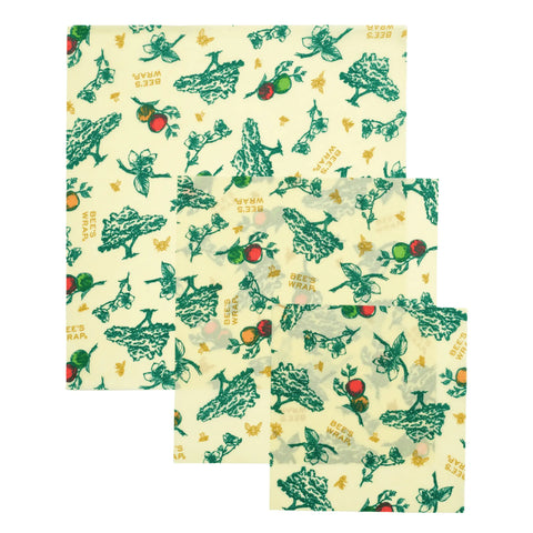 The Bees Wrap Assorted 3 Pack includes three square, reusable, plastic-free beeswax food wraps with green and gold nature prints of leaves, bees, and vegetables on a white background to help keep food fresh.