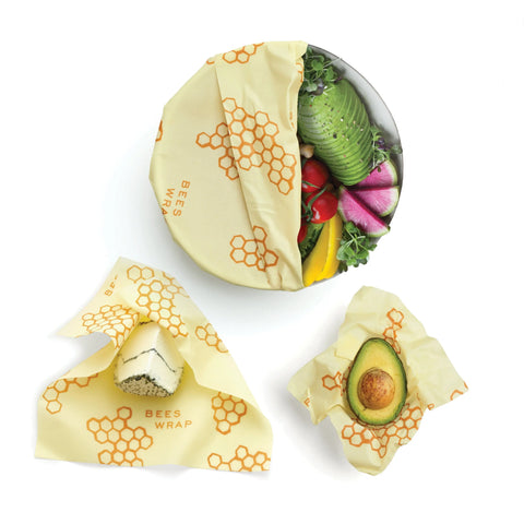 Three foods—a bowl of veggies, a cheese wedge, and half an avocado—are kept fresh in Bees Wrap Assorted 3 Pack: yellow, plastic-free wraps with orange honeycomb patterns.
