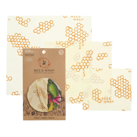 Three Bees Wrap reusable food storage wraps—plastic-free and decorated with honeycombs and bees—are shown with brown cardboard packaging. The Assorted 3 Pack keeps food fresh sustainably and stylishly.