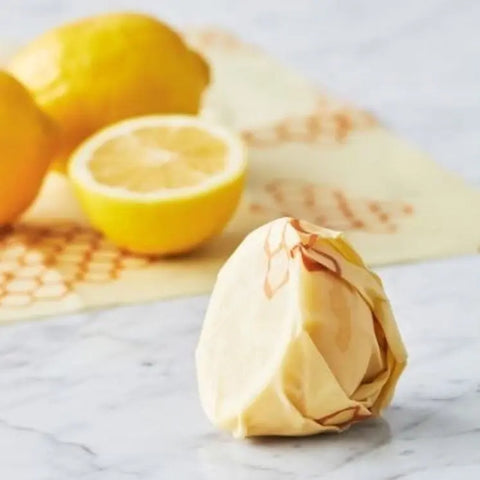 A halved and whole lemon rest on marble as another stays fresh in Bees Wrap, the plastic-free, reusable food wrap—perfect for storing produce with our Assorted 3 Pack.