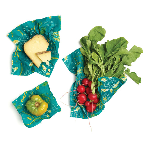 Keep cheese, a green tomato, and radishes fresh without plastic using the Bee’s Wrap Assorted 3 Pack—colorful beeswax wraps with a blue and yellow sea life pattern.