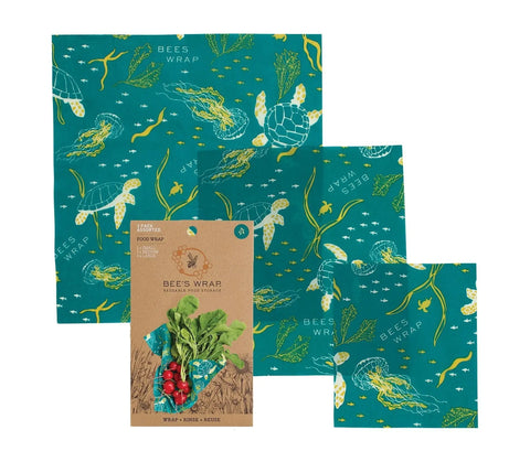 Bees Wrap Assorted 3 Pack features reusable food wraps with a blue ocean-themed design of sea turtles and jellyfish. The plastic-free wraps, shown packaging radishes, help keep your food fresh.