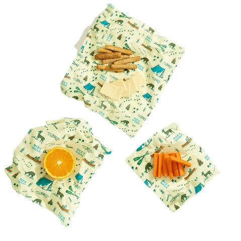 Keep food fresh with the Bees Wrap Assorted 3 Pack, a plastic-free set of beeswax food wraps in a camping pattern, shown holding orange slices, carrot sticks, crackers, and cheese on a white background.