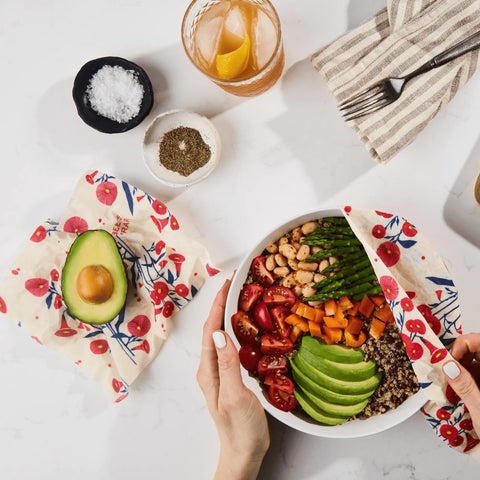 A person unwraps a fresh salad using Bees Wrap Assorted 3 Pack, showcasing a plastic-free way to enjoy avocado, cherry tomatoes, beans, asparagus, carrots, and quinoa—sustainable food storage from Bees Wrap.