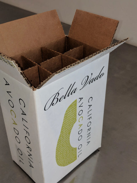A white Bella Vado Avocado Oil box labeled Case of Conventional Oil (6 Bottles) - 10% Discount is open to show cardboard dividers, sitting on a metallic surface.