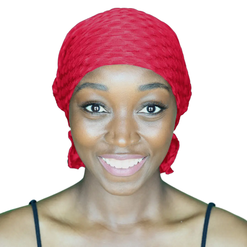 A smiling woman in a bright red Chemo Beanies® Kendall scarf and a black top looks directly at the camera against a plain background.