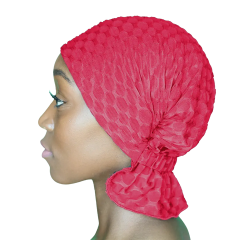 Profile view of a woman wearing the Scarves - Chemo Beanies® - Kendall by Chemo Beanies®, a textured red headwrap often used as a chemo beanie or head cover. Her head is turned left, highlighting smooth skin and long eyelashes on a transparent background.