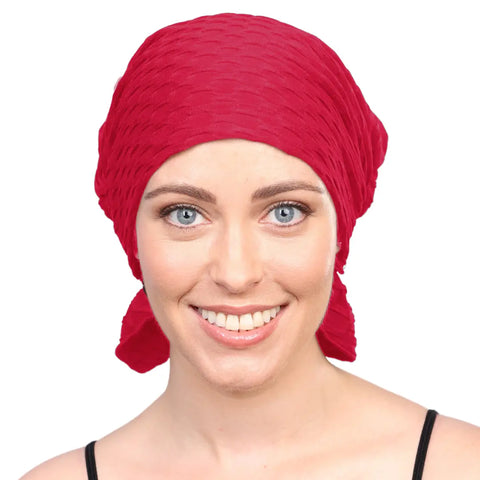 A smiling woman wears the Chemo Beanies® Kendall textured red chemo beanie, modeling this stylish cancer headwear with confidence against a plain white background.