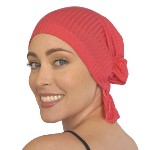 A smiling woman with light skin and blue eyes wears a Chemo Beanies® Scarves - Scarlet beanie tied at the back, looking over her shoulder against a plain background.