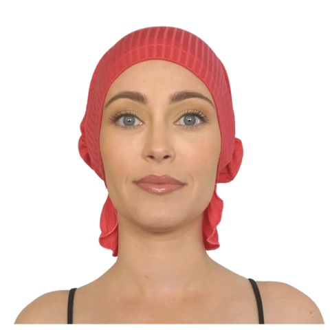 A woman faces forward against a plain black background, wearing the Chemo Beanies® Scarlet chemo beanie with natural makeup and a neutral expression.