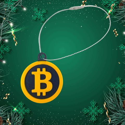 The Bitcoin Christmas Ornament by Chatelet Manufacturing features yellow and black colors, hangs from a silver string amid green pine branches and gold accents—ideal for cryptocurrency fans. Decorative holiday ornament. Made in the USA.