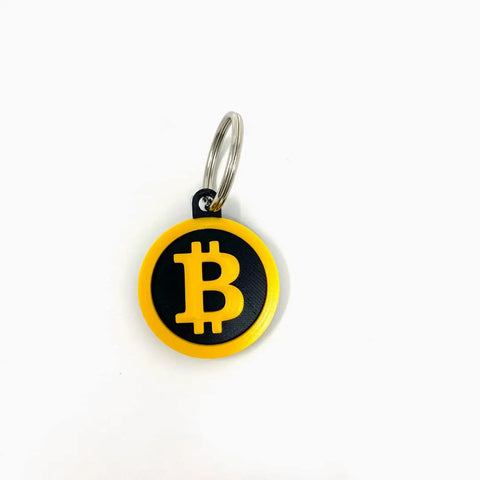 The Bitcoin Keychain by Chatelet Manufacturing features a yellow symbol on black with a yellow outline, attached to a metal ring. Ideal for cryptocurrency fans, it’s proudly made in the USA and shown on a plain white surface.