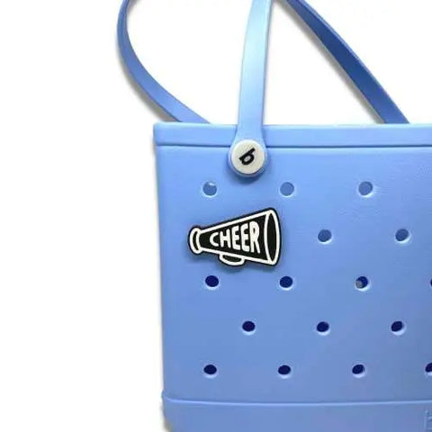 A Chatelet Manufacturing BOGLETS black megaphone charm saying CHEER attaches to Bogg Bags, making it perfect for cheer teams. Add this stylish accessory to your light blue tote with perforated holes and two top handles.