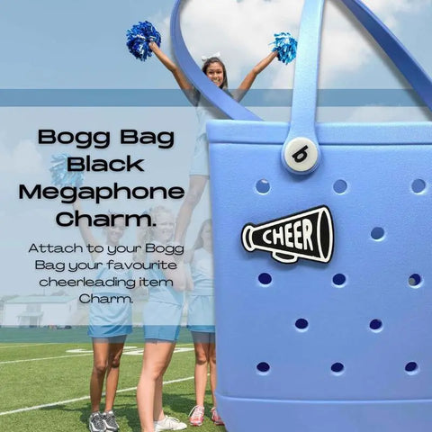 A blue Bogg Bag featuring the Chatelet Manufacturing BOGLETS Black Megaphone Charm is in the foreground, while cheer teams in blue uniforms perform stunts on a grassy field. Text highlights details of the bag charm.